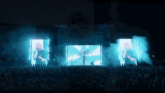 a crowd of people watching a concert with a large screen behind them that says ' a ' on it
