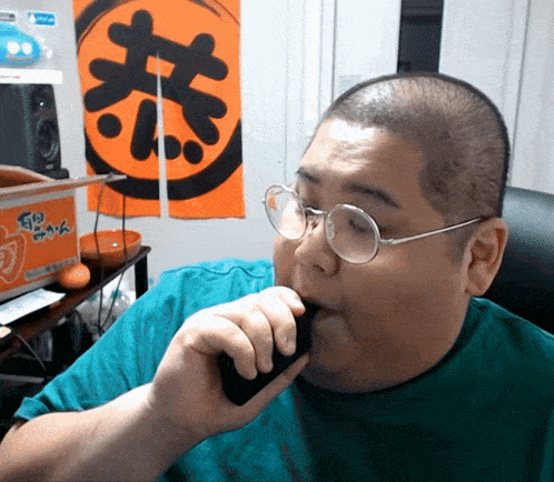 a man wearing glasses and a green shirt is smoking a cigarette in front of an orange sign that says go