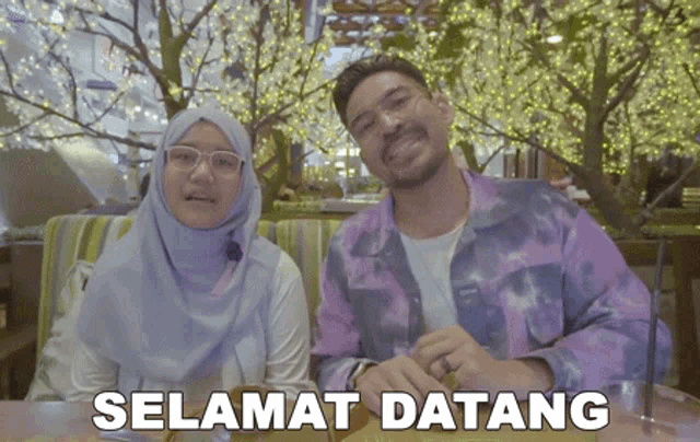 a man and a woman are sitting at a table with the words selamat datang written on the bottom