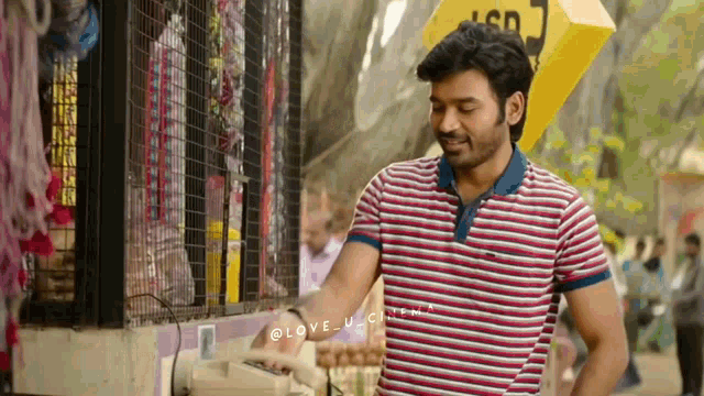 a man in a striped shirt is standing in front of a store holding a telephone .