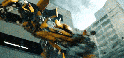 a yellow transformer is flying through the air in front of a building .