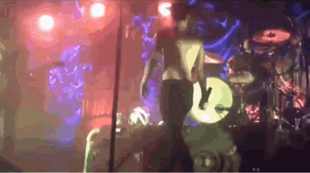 a woman stands on a stage in front of a drum kit
