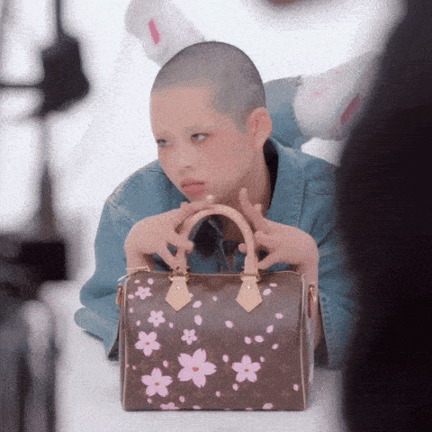 a woman with a shaved head is holding a louis vuitton bag with pink flowers on it