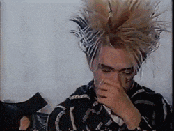 a person with a mohawk covering their nose with their hand