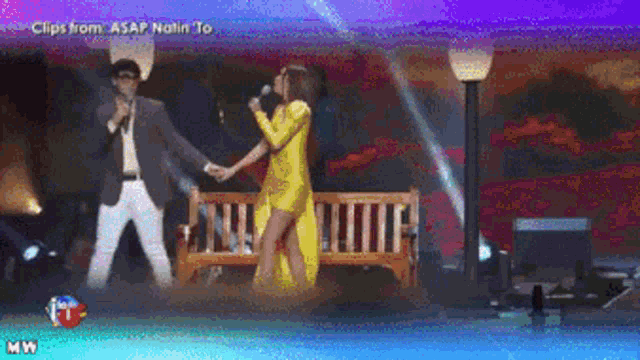 a man in a suit and a woman in a yellow dress are singing on stage