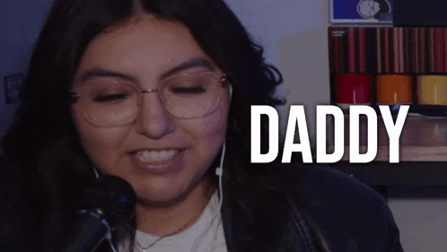 a woman with glasses is singing into a microphone with the word daddy behind her
