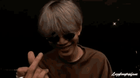 a man wearing sunglasses and a brown shirt is laughing with his mouth open .