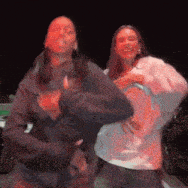 two women are dancing in front of a car at night .
