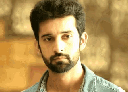 a man with a beard is wearing a blue denim shirt