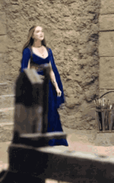 a woman in a blue dress stands next to a stone wall