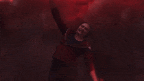 a person in a red shirt is standing in front of a fire in the dark .