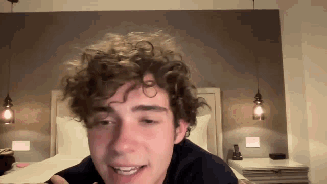 a young man with curly hair is laying on a bed and smiling