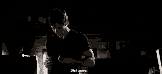 a man in a black shirt is standing in a dark room and talking to another man .