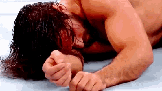a shirtless wrestler is laying on the floor with his head on the ground .