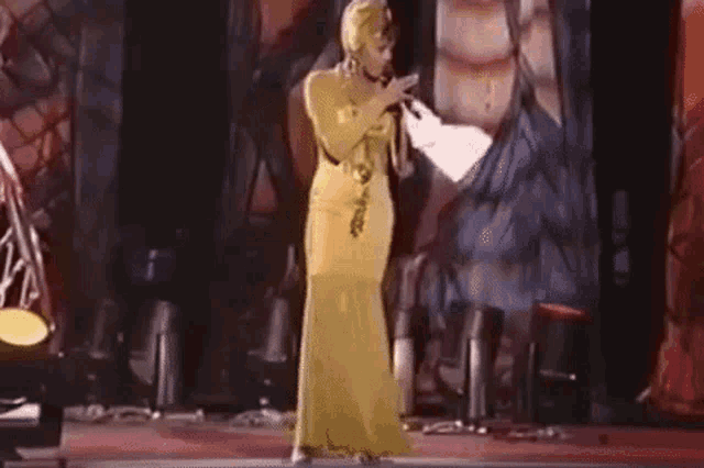a woman in a yellow dress is singing into a microphone on stage .