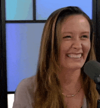 a woman is smiling in front of a microphone and looking at the camera .