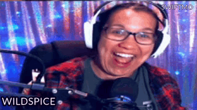 a woman wearing headphones and glasses is smiling in front of a microphone and the word wildspice is on the screen