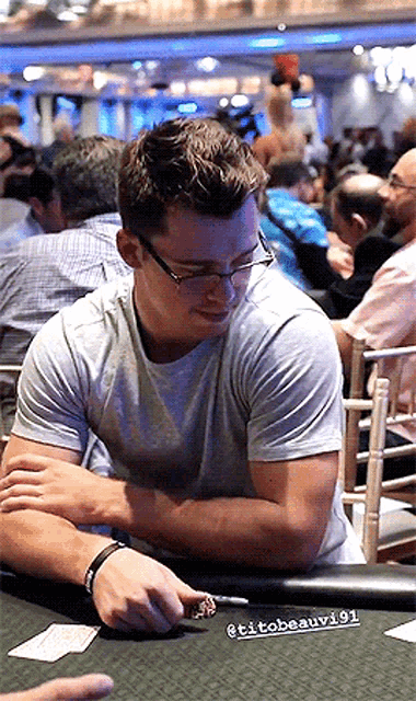 a man wearing glasses sits at a poker table with the name tito beauvi91 written on it