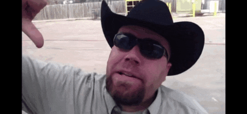 a man wearing a cowboy hat and sunglasses giving the thumbs down sign