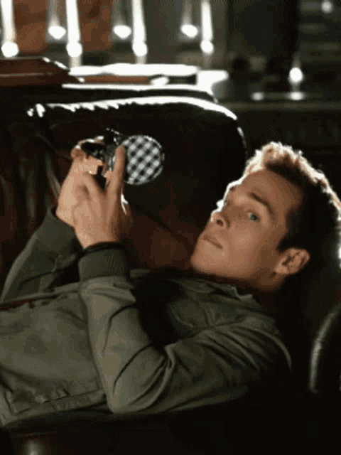 a man in a green jacket is laying on a leather couch holding a pair of binoculars