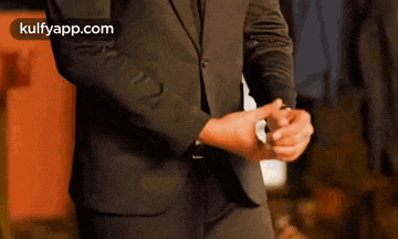 a man in a suit is adjusting his cuffs while wearing a watch .