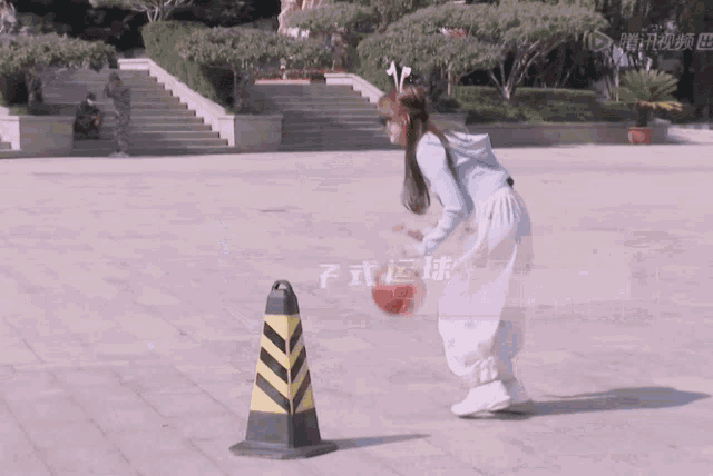 a woman is throwing a basketball in front of a yellow and black traffic cone
