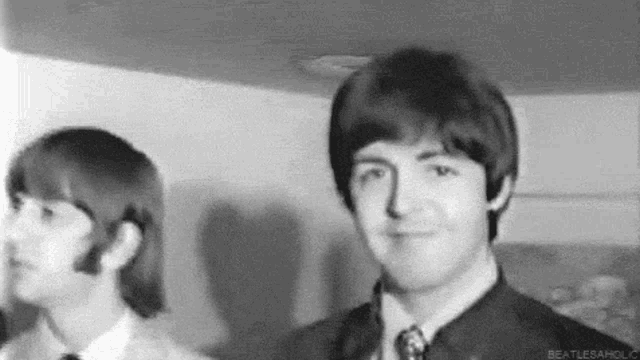 a black and white photo of a man in a suit and tie standing next to another man .