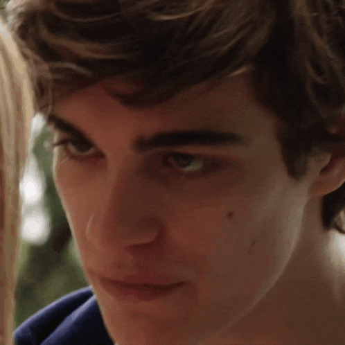 a close up of a young man 's face with a woman behind him
