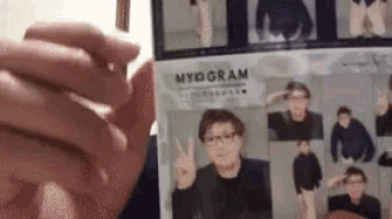 a person is holding a picture of a man with glasses and giving a peace sign .