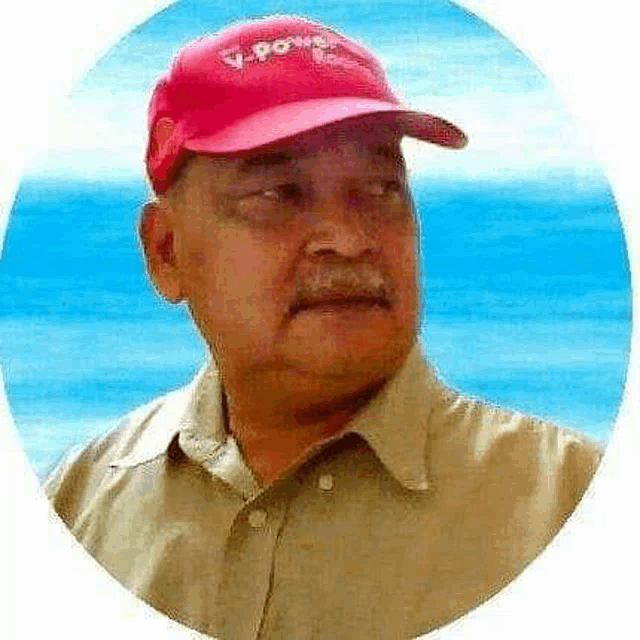 a man wearing a red hat and a tan shirt is standing in front of a blue ocean .