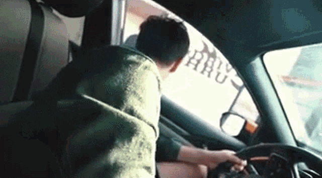 a man in a green hoodie is driving a car with a sticker on the window that says bravo aru
