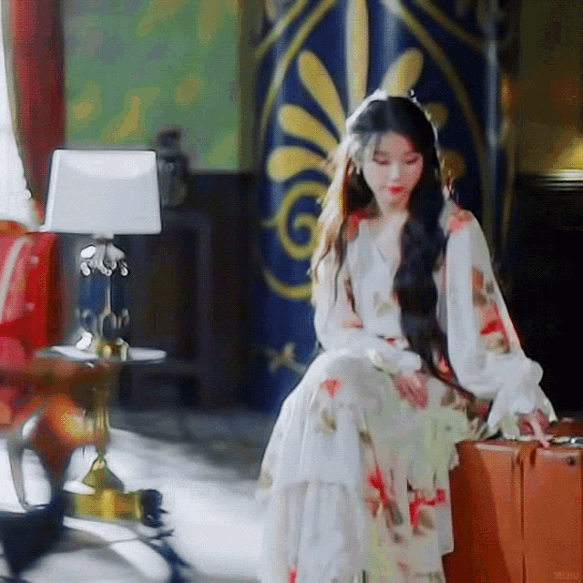 a woman in a floral dress is sitting on a suitcase