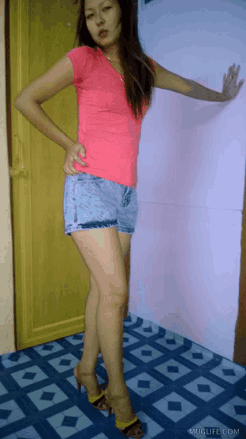 a woman wearing a pink shirt and shorts is standing in front of a muglife.com sign