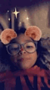 a little girl wearing glasses and a red nose is taking a selfie .