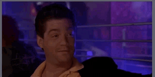 a man is making a funny face while holding his hands up in front of a purple wall .
