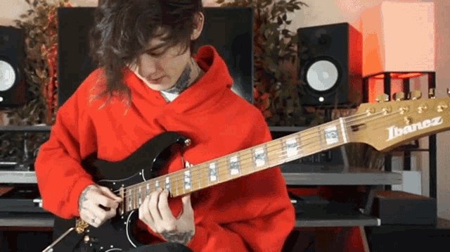 a man in a red hoodie plays an ibanez electric guitar