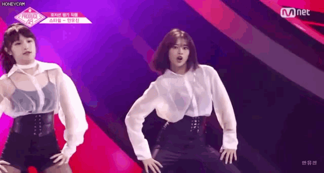 two women are dancing on a stage in front of a purple background .
