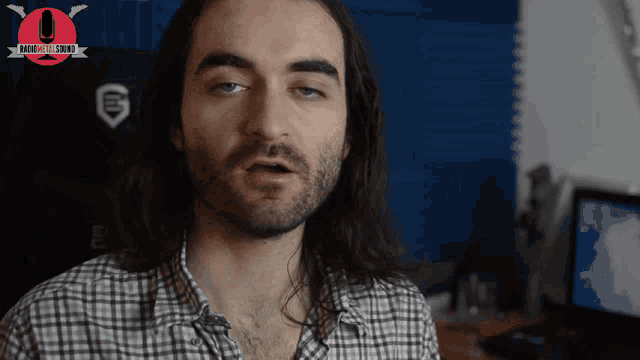 a man with long hair and a beard is sitting in front of a microphone and a sign that says radio real sound