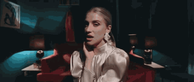 a woman in a white dress is sitting in a red chair in a dark room