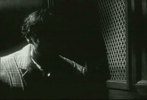 a black and white photo of a man behind a metal fence