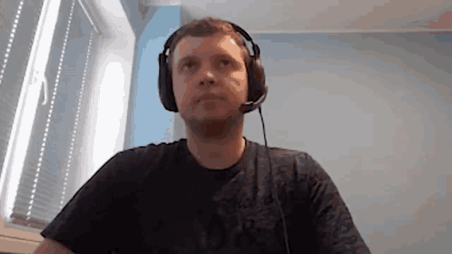 a man wearing headphones and a microphone is sitting at a desk in front of a window .