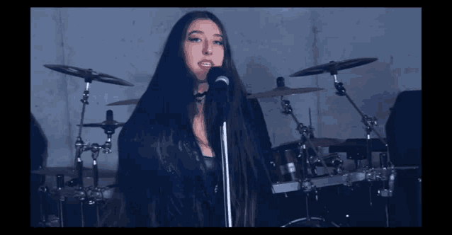 a woman singing into a microphone with drums in the background