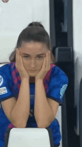 a woman in a blue shirt is sitting on a bench with her head resting on her hands .