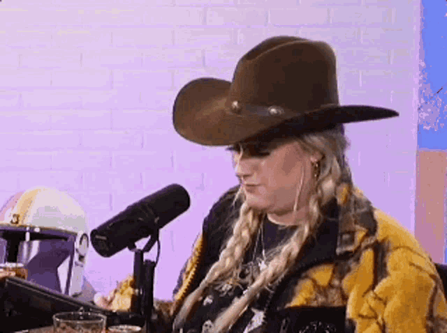 a woman wearing a cowboy hat and a yellow jacket is sitting at a table in front of a microphone .