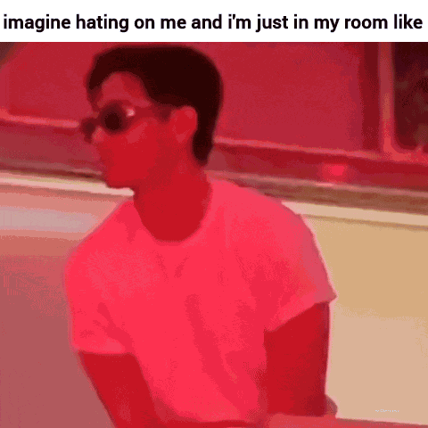 a man wearing sunglasses and a pink shirt is sitting in a room with a red background .