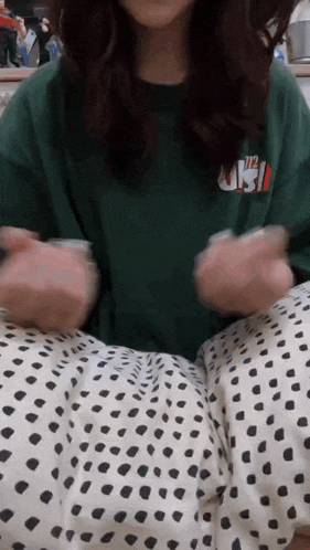 a woman wearing a green t-shirt and polka dot pants is sitting on a bed .