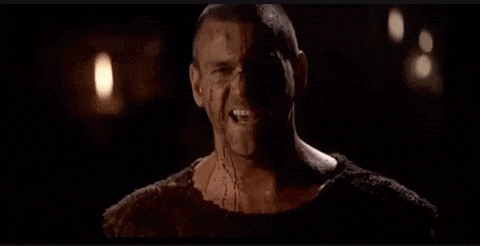 a man with a tattoo on his face is standing in the dark .