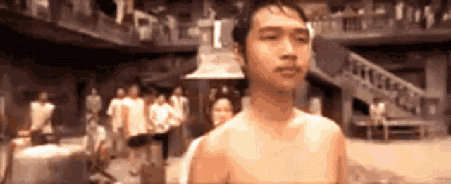 a shirtless man is standing in front of a crowd of people in a room .