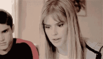 a man and a woman are sitting next to each other in a room and the woman is looking at the camera .