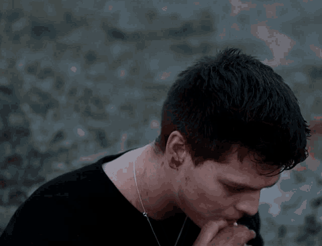 a young man wearing a black shirt and a necklace looks down